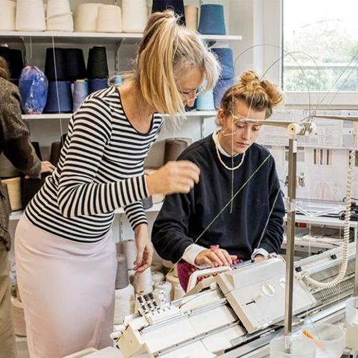 Lehrerin zeigt einer Schülerin etwas an der Strickmaschine