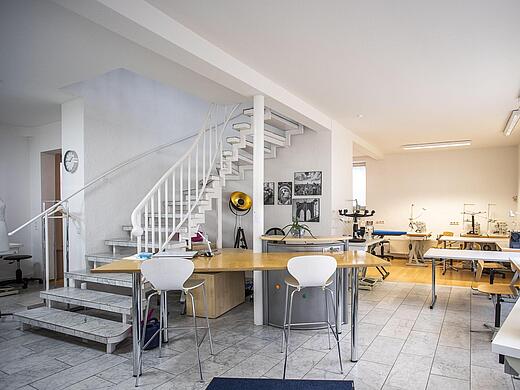 Nähatelier Start-Up - Eingangsbereich mit Treppe nach oben, Nähmaschinen, Stühlen und dem Lehrerpult.