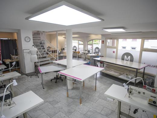 Nähatelier Start-Up - Unterrichtsbereich mit großem Schnitttisch in der Mitte und am Fester, sowie Nähmaschinen an der Wand.