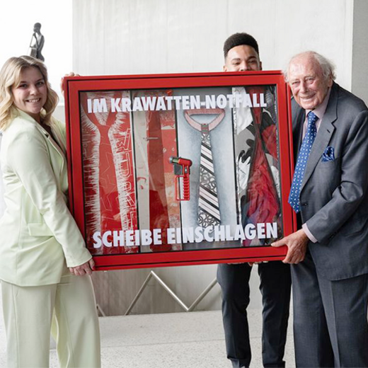 eine junge Frau und ein ältere Herr die einen Schaukasten mit Krawatten halten